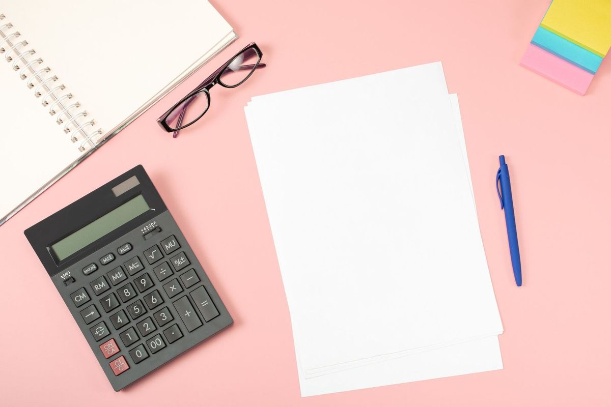 Office flat lay. Blank white sheet of paper with pen are on top of pink office desk table with calculator and suplpies.