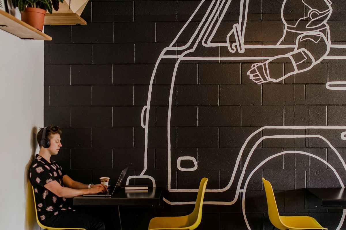 man wearing headphone using laptop while sitting beside table inside cafe